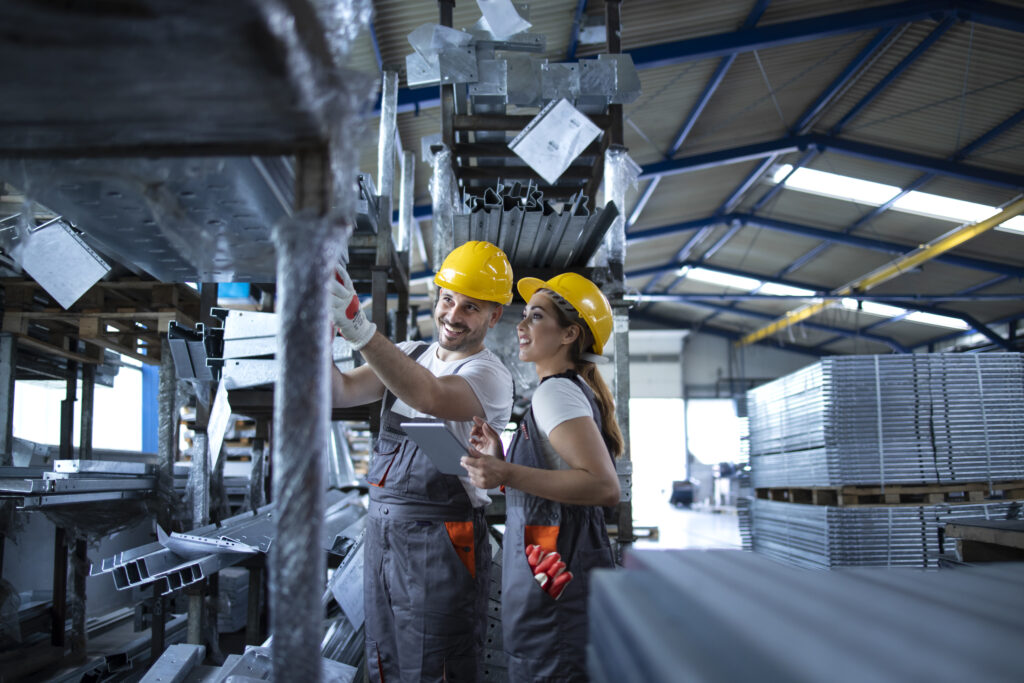 Operarios revisando inventario con tableta en bodega industrial de piezas metálicas