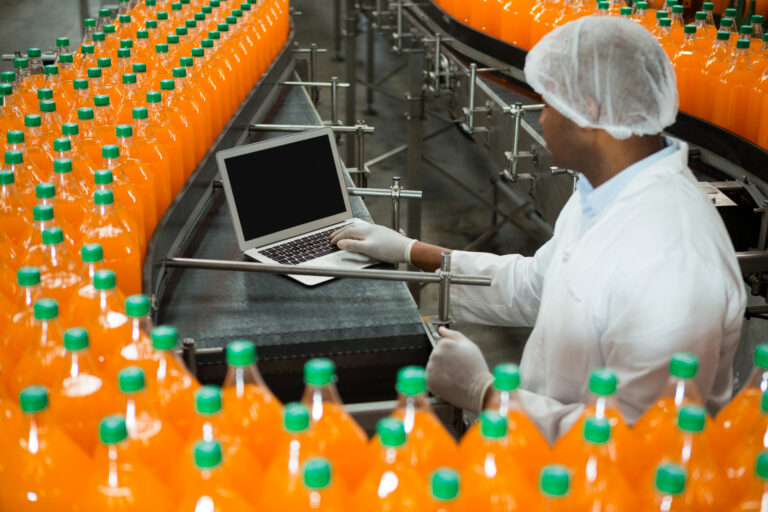 Operario con computador portátil junto a la línea de producción de una planta de bebidas