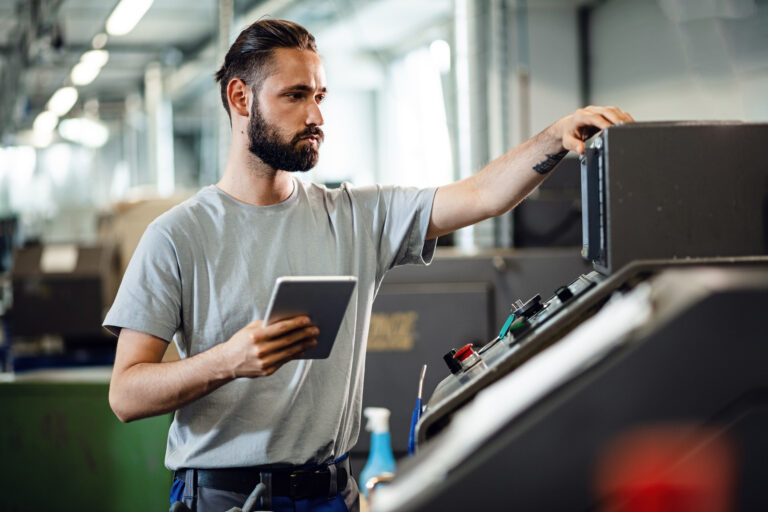 Operario con una tableta junto a una máquina industrial en un taller metalmecánico